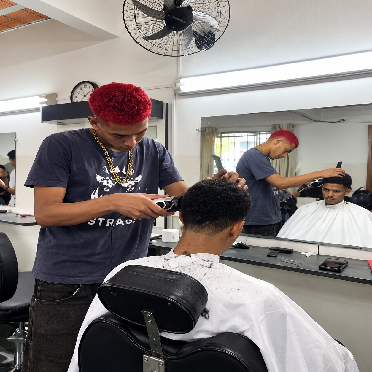 Profissional cortando o cabelo de um cliente em uma barbearia, com espelho refletindo o ambiente