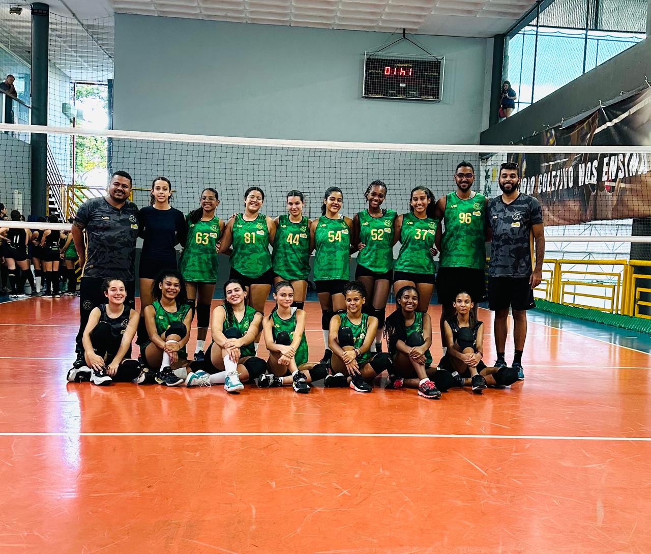 Equipe de vôlei do GDECOM reunida em quadra, com adolescentes e educadores usando uniformes verdes
