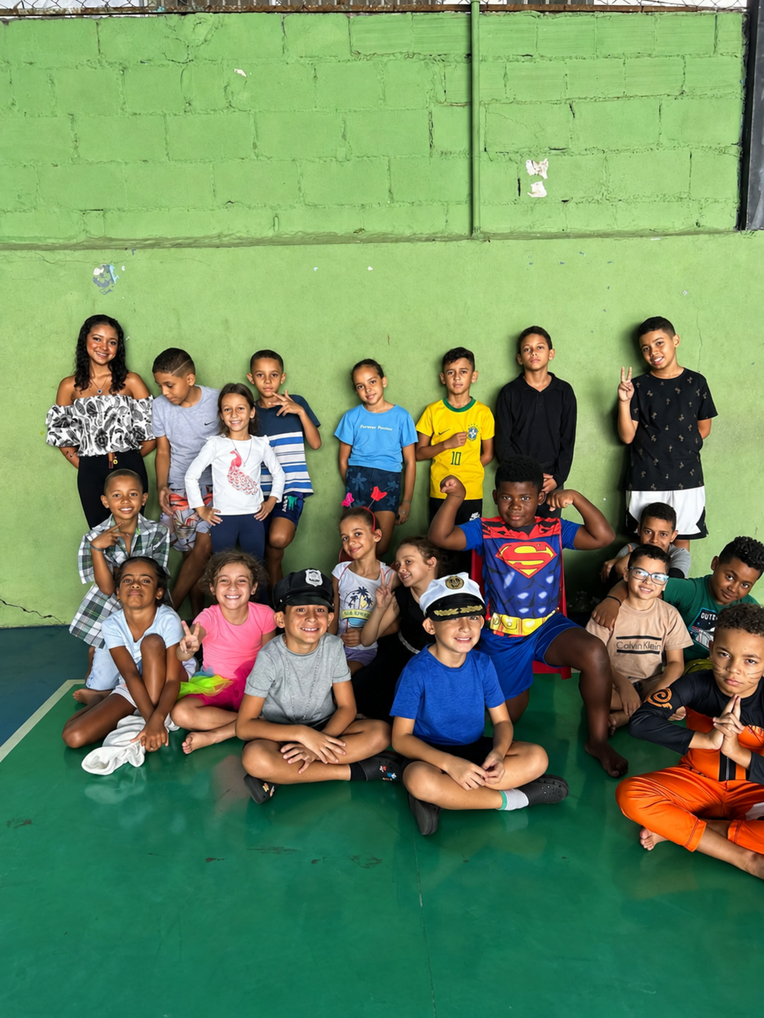 Grupo grande de crianças reunidas e sorrindo em quadra esportiva, algumas fantasiadas em dia temático